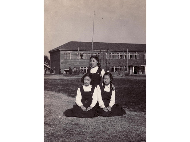 坐昭和20年頃の旧世田谷キャンパスの校庭、正門前で友達との写真　左手前が千江子さん