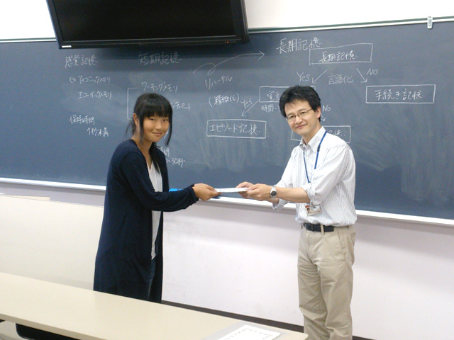大学院臨床心理学専攻主任の松岡先生から賞状を授与されにっこり。副賞のシャープペンシルは、検定でマークシートを塗る時に使ってくださいね！